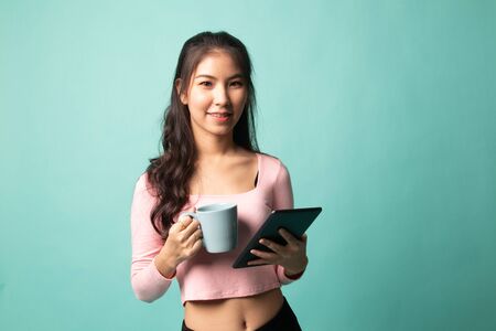 Young Asian woman with a computer tablet and coffee on cyan backgroundの写真素材
