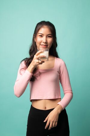 Healthy Asian woman drinking a glass of milk on cyan backgroundの写真素材