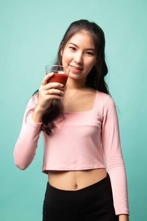 Young Asian woman drink tomato juice on cyan backgroundの写真素材