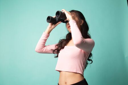 Young Asian woman with binoculars on cyan backgroundの写真素材