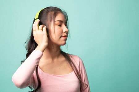 Pretty asian girl listening music with her headphones on cyan backgroundの写真素材