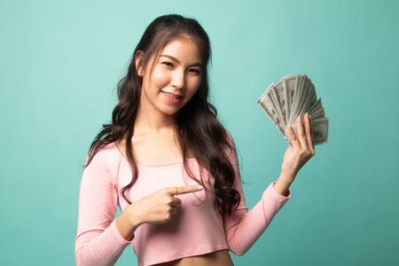 Portrait of  young asian woman  showing bunch of money banknotes on cyan backgroundの写真素材