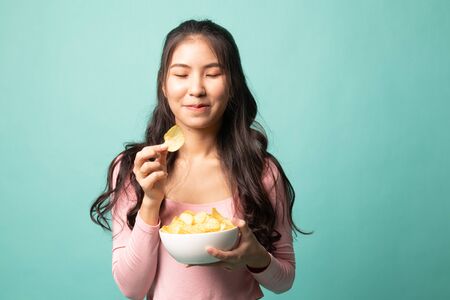 Young Asian woman eat potato chips on cyan backgroundの写真素材