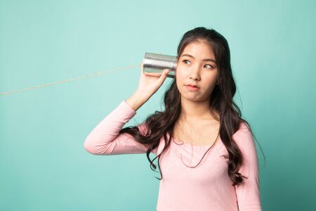 Young Asian woman with tin can phone on cyan backgroundの写真素材