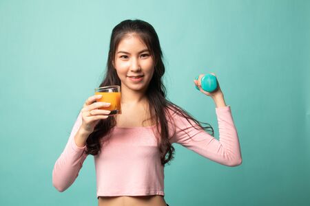 Young Asian woman with dumbbell drink orange juice on cyan backgroundの写真素材