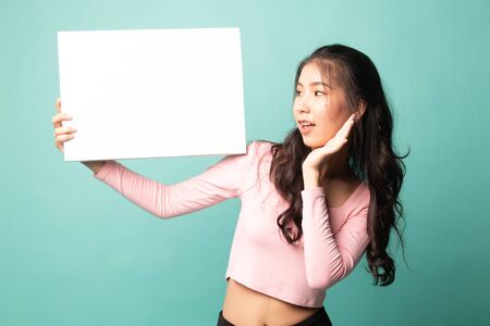 Young Asian woman  surprise with  white blank sign on cyan backgroundの写真素材