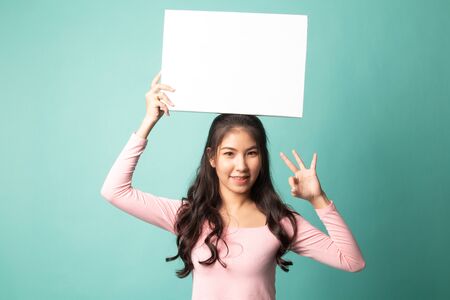 Young Asian woman show OK with  white blank sign on cyan backgroundの写真素材