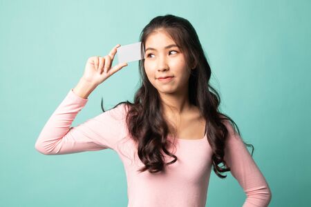 Young Asian woman think with a blank card on cyan backgroundの写真素材