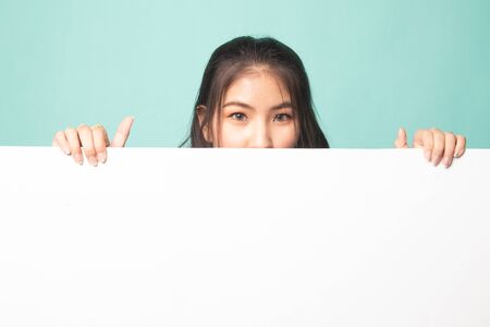 Close up of young Asian woman behind a blank sign on cyan backgroundの写真素材