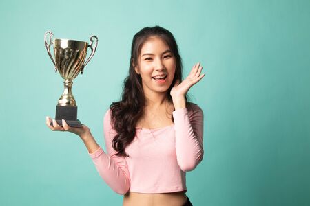 Successful young asian woman holding a trophy on cyan backgroundの写真素材