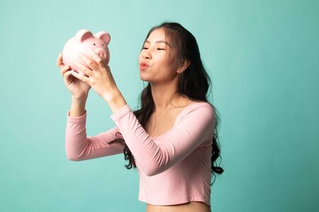 Young Asian woman kiss  a pink coin bank on cyan backgroundの写真素材