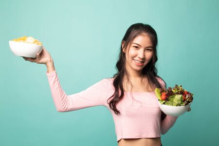 Young Asian woman with potato chips and salad on cyan backgroundの写真素材