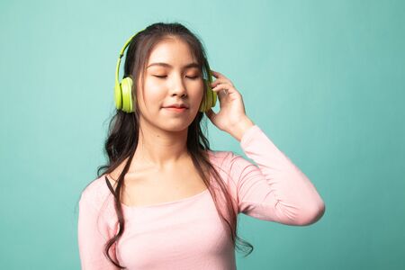 Pretty asian girl listening music with her headphones on cyan backgroundの写真素材