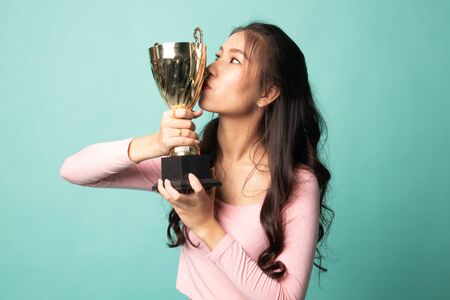Successful young asian woman holding kissing a trophy on cyan backgroundの写真素材