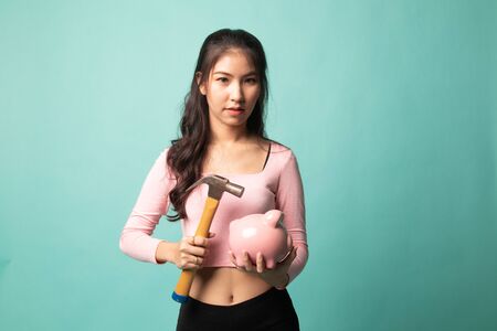 Asian woman with pig coin bank and hammer on cyan backgroundの写真素材