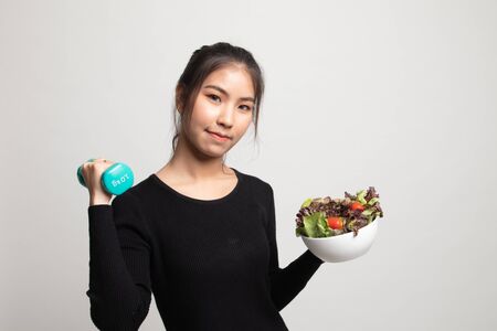 Healthy Asian woman with dumbbells and salad on white backgroundの写真素材