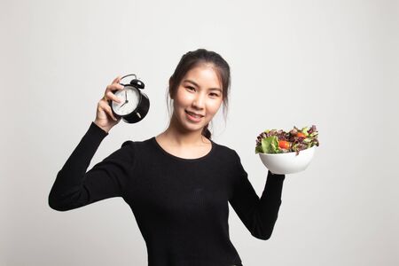 Young Asian woman with clock and salad on white backgroundの写真素材