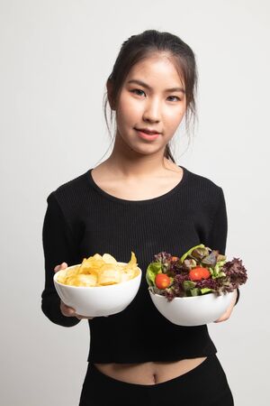 Young Asian woman with potato chips and salad on white backgroundの写真素材