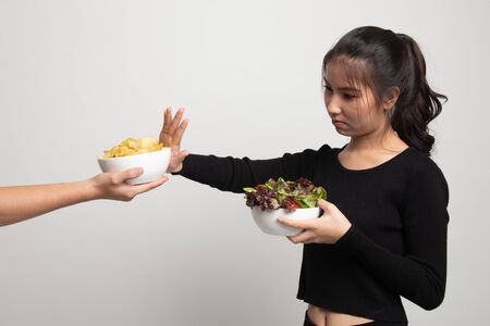 Young Asian woman with salad say no to potato chips on white backgroundの写真素材