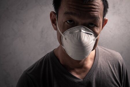Asian man wearing N95  mask to prevent flu virus and  PM2.5 dust air pollution on gray concrete backgroundの写真素材