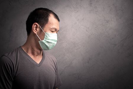 Asian man  wearing surgical  mask to prevent flu virus and  PM2.5 dust air pollution on gray concrete backgroundの写真素材