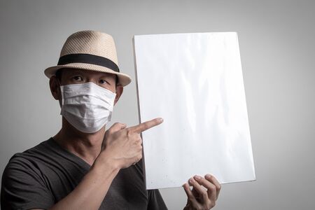 Asian man  wearing surgical  mask to prevent flu virus and  PM2.5 dust air pollution with white blank sign on white backgroundの写真素材
