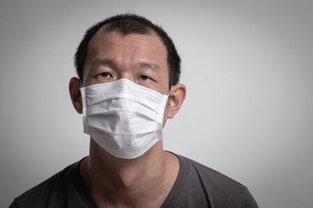 Asian man  wearing surgical  mask to prevent flu virus and  PM2.5 dust air pollution on white backgroundの写真素材