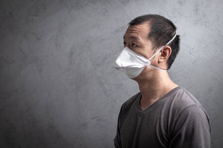 Asian man wearing surgical  mask to prevent flu virus and  PM2.5 dust air pollution  on gray concrete backgroundの写真素材