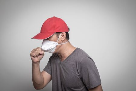 Sick Asian man in red hat coughing and  wearing surgical  mask to prevent flu virus and  PM2.5 dust air pollution on white backgroundの写真素材