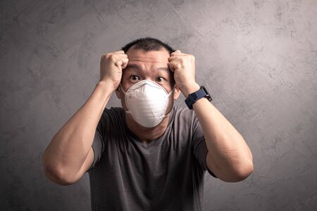 Asian man wearing N95  mask to prevent flu virus and  PM2.5 dust air pollution on gray concrete backgroundの写真素材