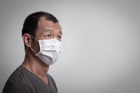 Asian man  wearing surgical  mask to prevent flu virus and  PM2.5 dust air pollution on white backgroundの写真素材