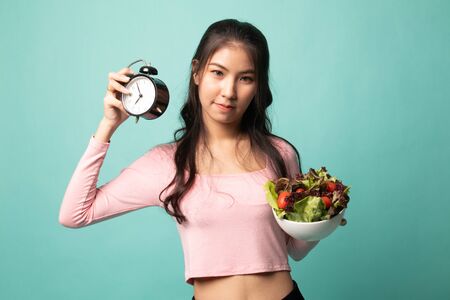 Young Asian woman with clock and salad on cyan backgroundの写真素材