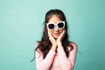 Portrait of a beautiful young asian girl in sunglasses on cyan backgroundの写真素材
