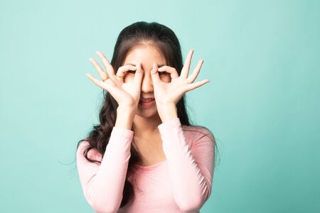 Asian woman do funny  double OK sign as glasses on cyan backgroundの写真素材