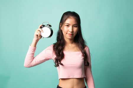 Young Asian woman with a clock on cyan backgroundの写真素材