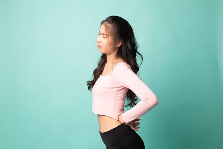 Young Asian woman got back pain on cyan backgroundの写真素材