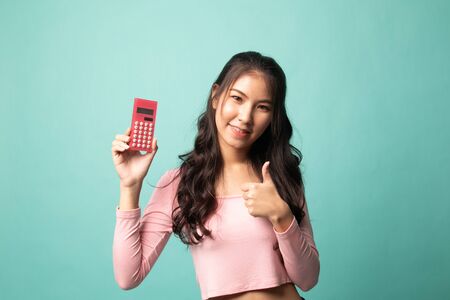 Asian woman thumbs up with calculator on cyan backgroundの写真素材