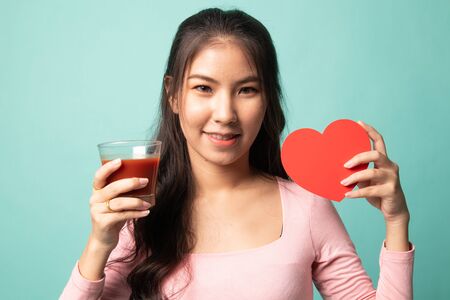 Young Asian woman with tomato juice and red heart on cyan backgroundの写真素材