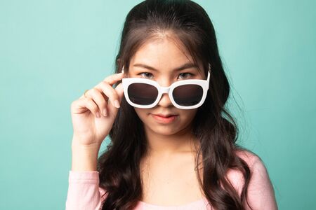 Portrait of a beautiful young asian girl in sunglasses on cyan backgroundの写真素材