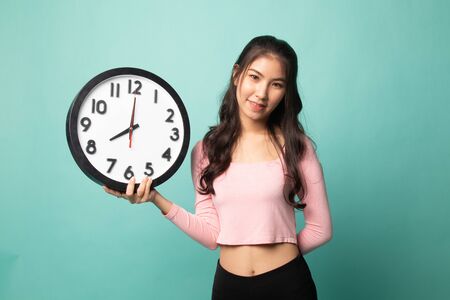 Young Asian woman with a clock on cyan backgroundの写真素材