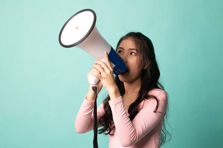 Beautiful young Asian woman announce with megaphone on cyan backgroundの写真素材