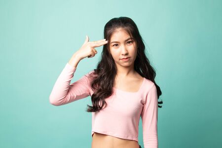 Beautiful young Asian woman holding fingers in gun gesture on cyan backgroundの写真素材
