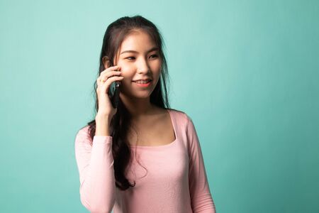 Young Asian woman talking with mobile phone on cyan backgroundの写真素材