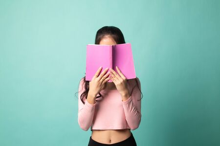 Young Asian woman with a book cover her face on cyan backgroundの写真素材