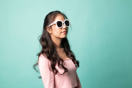 Portrait of a beautiful young asian girl in sunglasses on cyan backgroundの写真素材