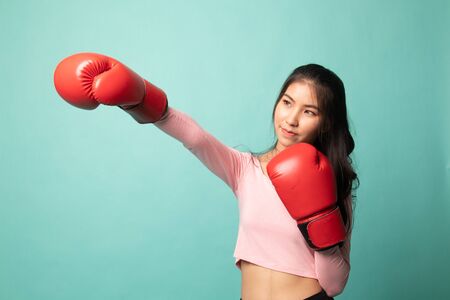 Young Asian woman with red boxing gloves on cyan backgroundの写真素材