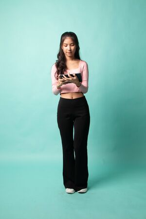 Full body of young Asian woman with a computer tablet on cyan backgroundの写真素材