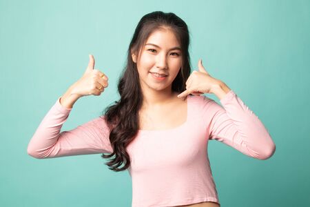 Young Asian woman thumbs up show with phone gesture on cyan backgroundの写真素材