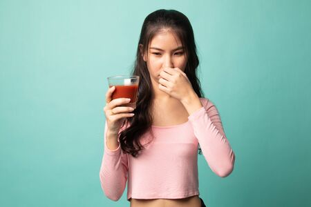 Young Asian woman hate tomato juice on cyan backgroundの写真素材
