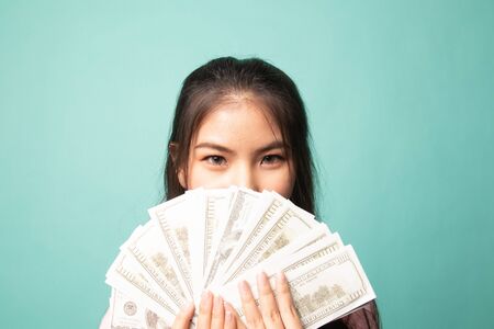 Portrait of  young asian woman  showing bunch of money banknotes on cyan backgroundの写真素材